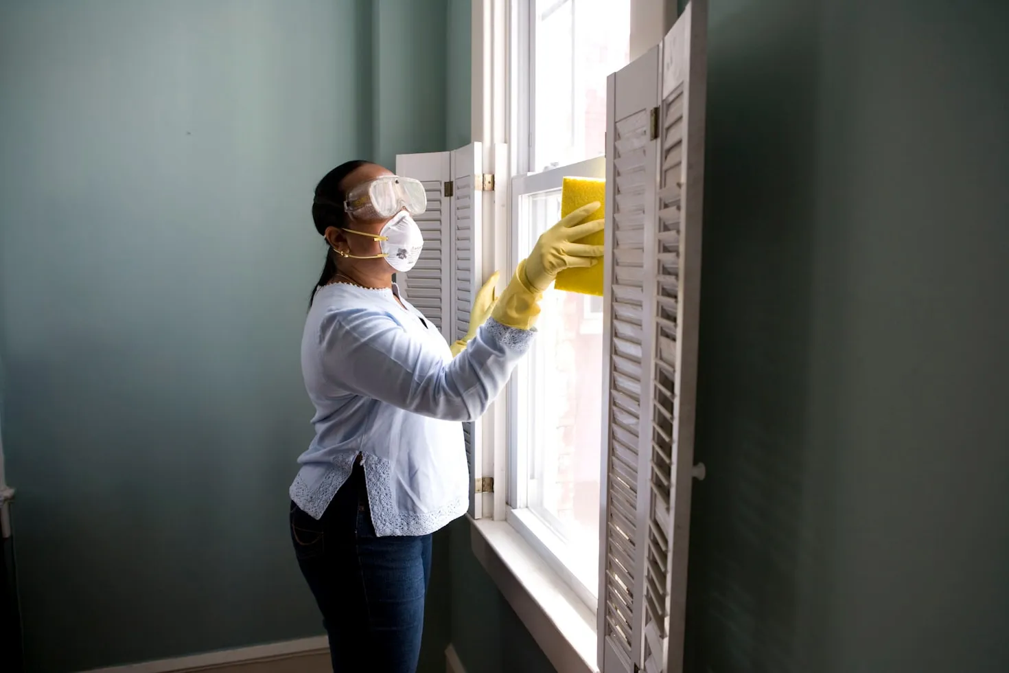 A person wearing blue gloves and using a squeegee to clean a glass window, symbolizing data cleaning.